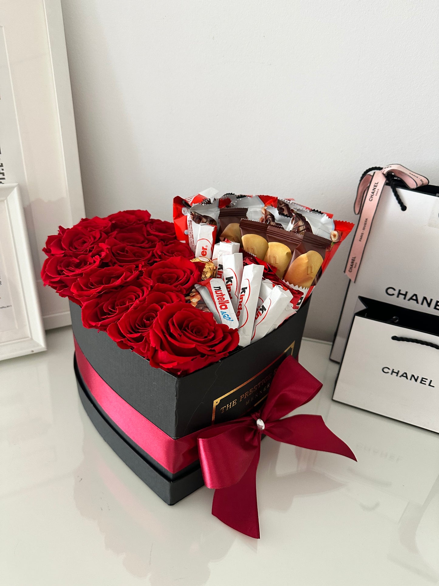 Arreglo floral de rosas rojas premium con chocolates Kinder y Ferrero en caja negra de lujo.