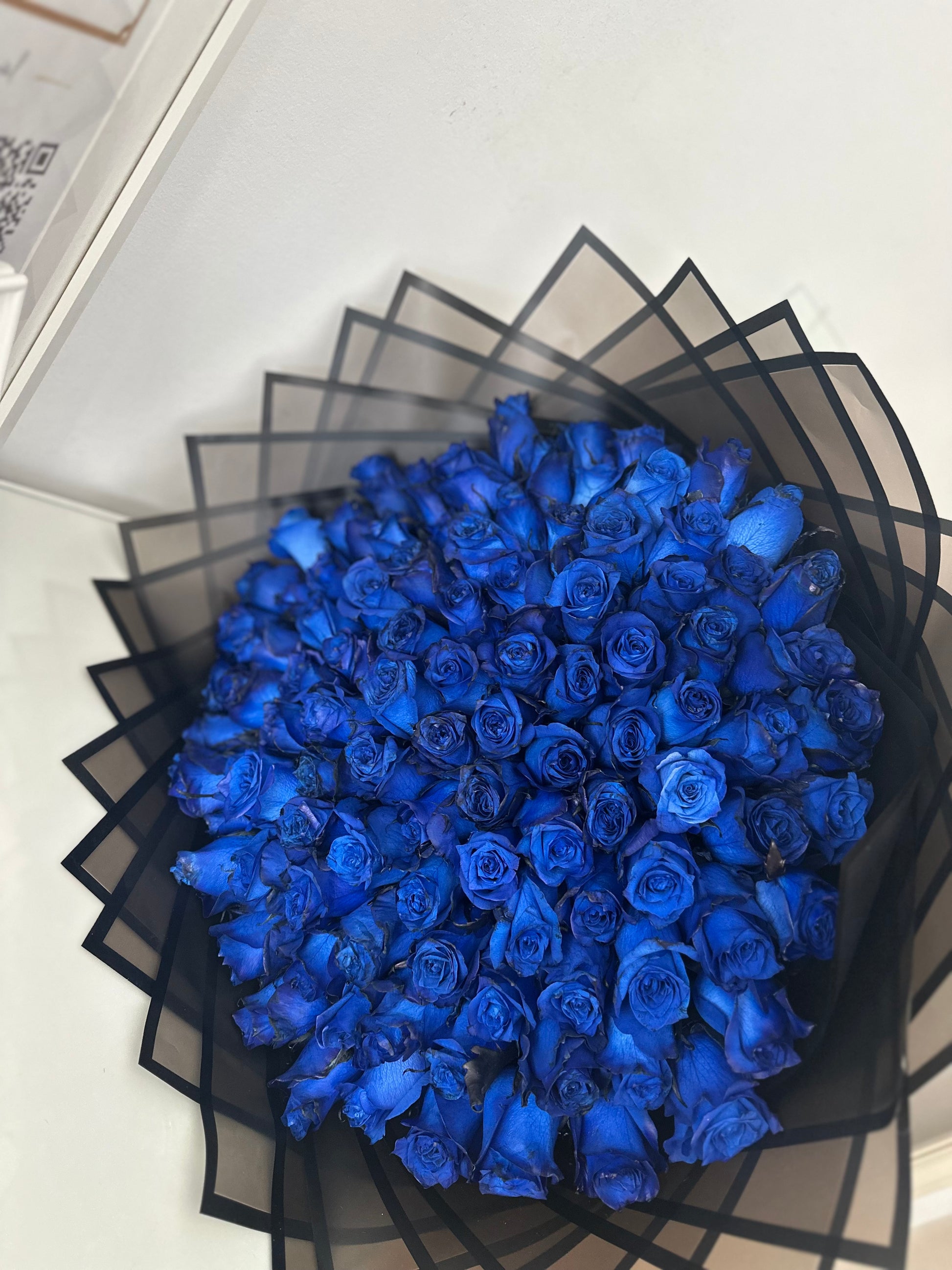 Ramo de 101 rosas azules naturales envueltas en elegante papel negro mate con lazo azul satinado, ideal para regalos exclusivos en Madrid.