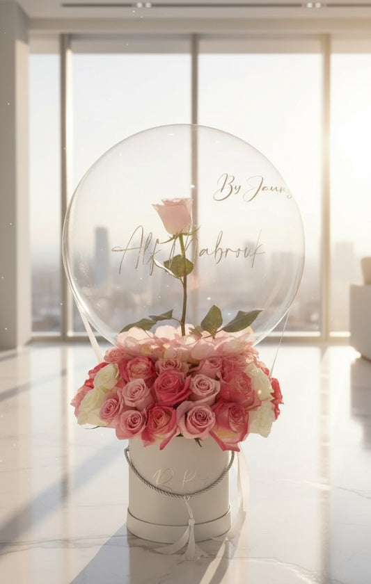 Arreglo de rosas rosas y blancas con globo transparente y una rosa única en el centro, diseño elegante en caja redonda blanca.