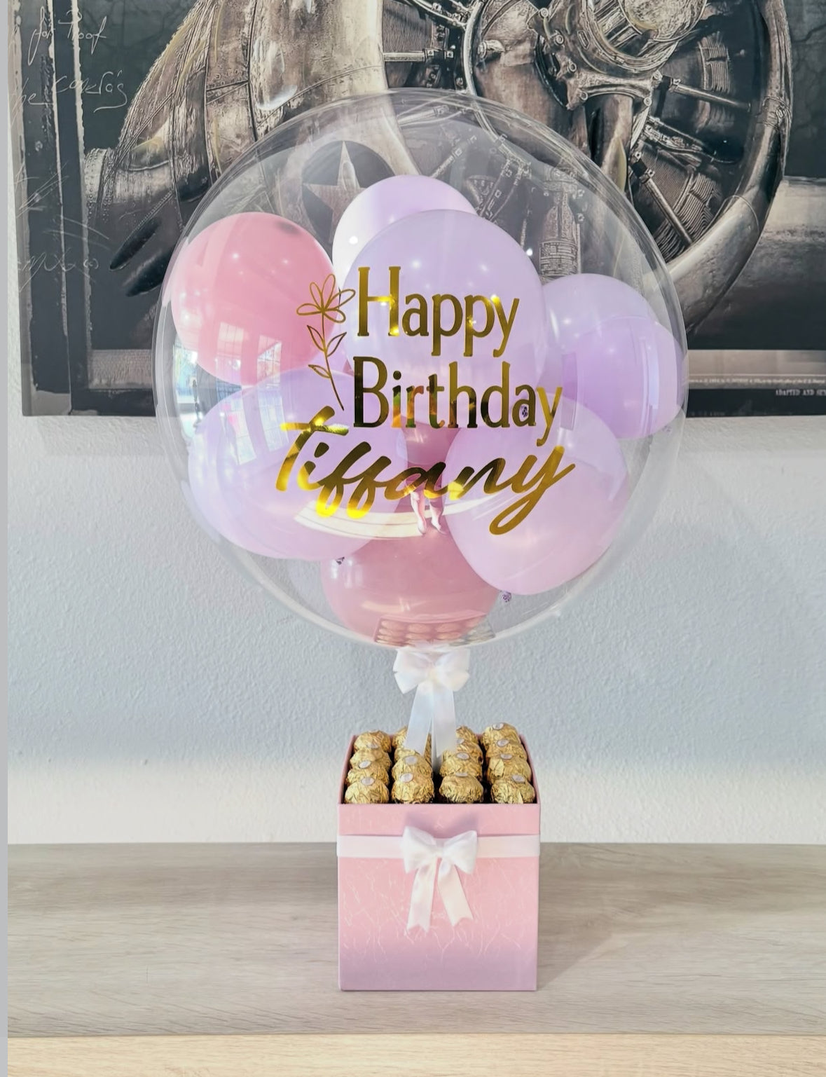 Set de regalo negro con globo transparente personalizado y mini globos dorados, decorado con lazo blanco y chocolates Ferrero Rocher – un detalle elegante de The Prestige Roses Madrid.
Black and gold personalized balloon gift box with white bow and Ferrero Rocher chocolates – a luxury and elegant detail by The Prestige Roses Madrid.