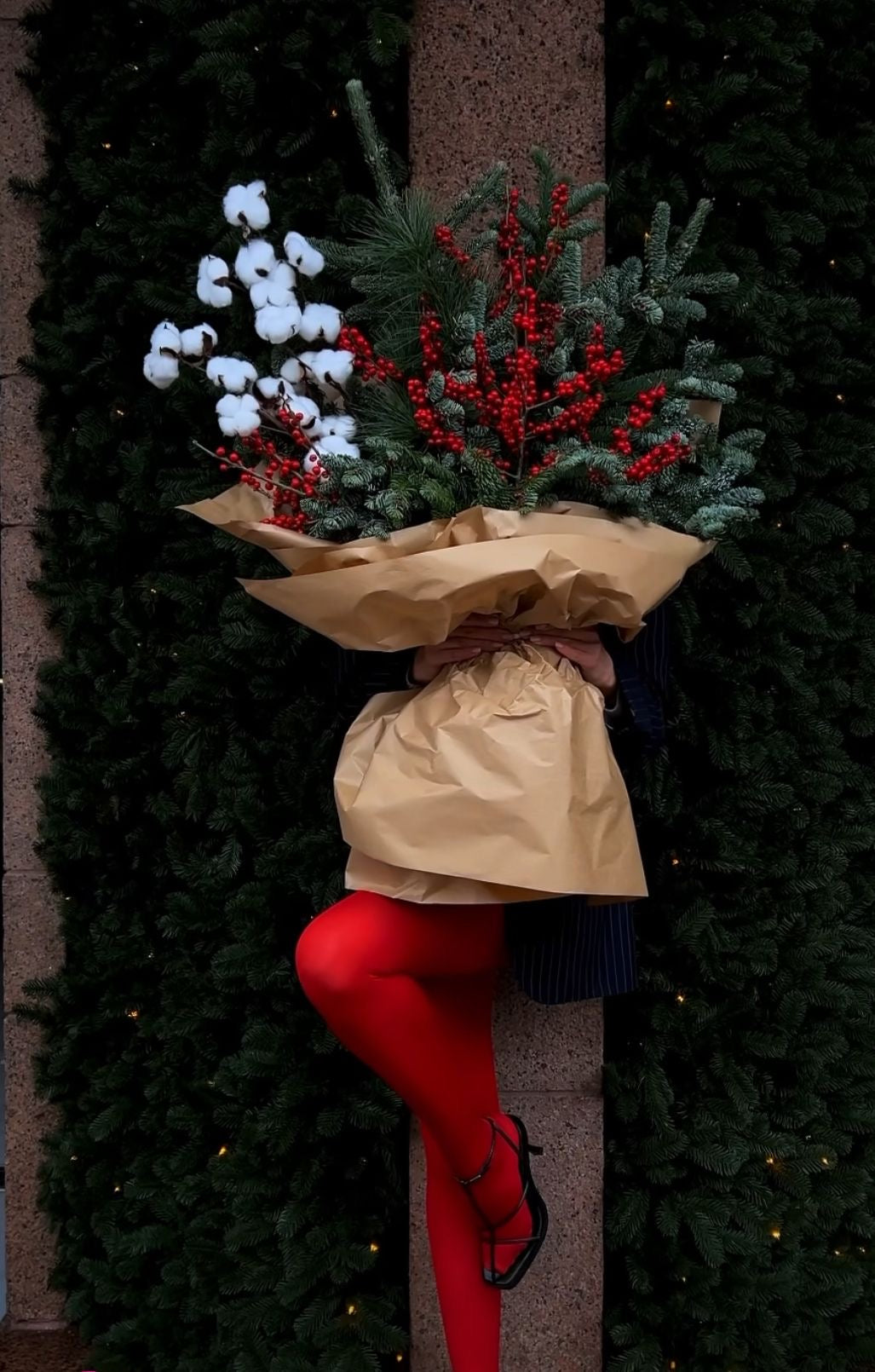 Arreglo floral navideño en base dorada con rosas crema, hojas de eucalipto y detalles festivos naturales.