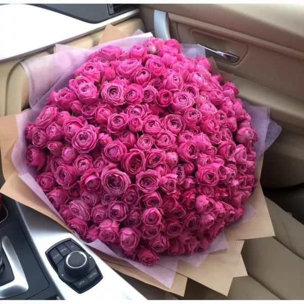 Ramo de 101 rosas premium en tono rosa intenso, presentado sobre asiento de coche de lujo. Bouquet of 101 premium pink roses placed on a luxury car seat.