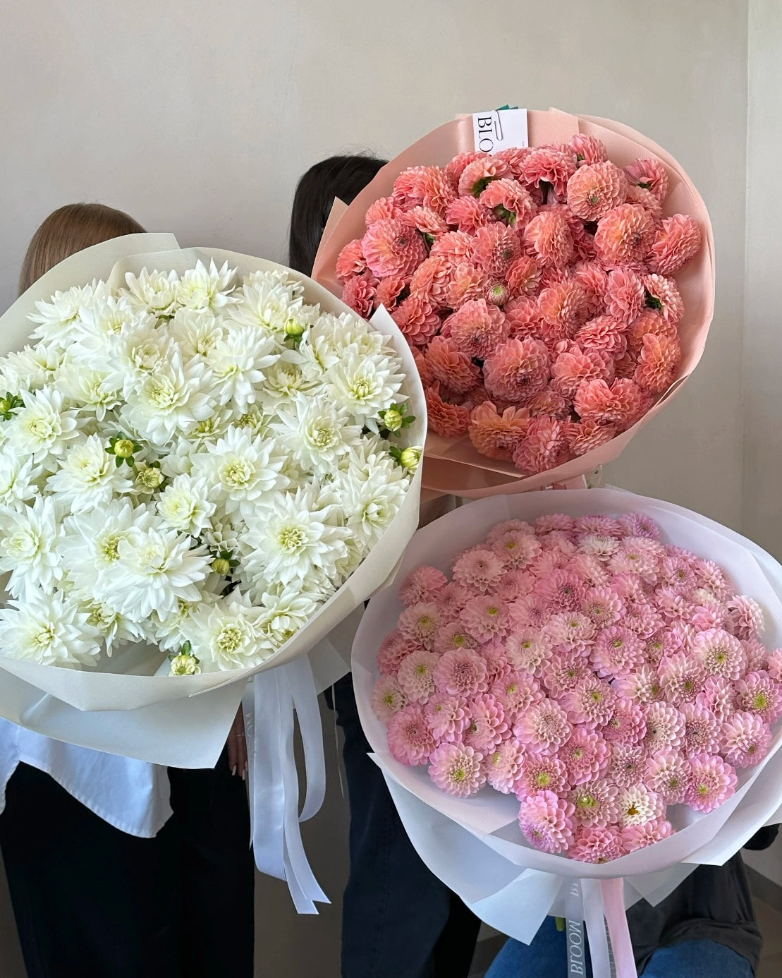 Tres ramos de dalias en tonos blanco, rosa y melocotón, envueltos en papel elegante con lazo de satén, creación artesanal de The Prestige Roses Madrid.