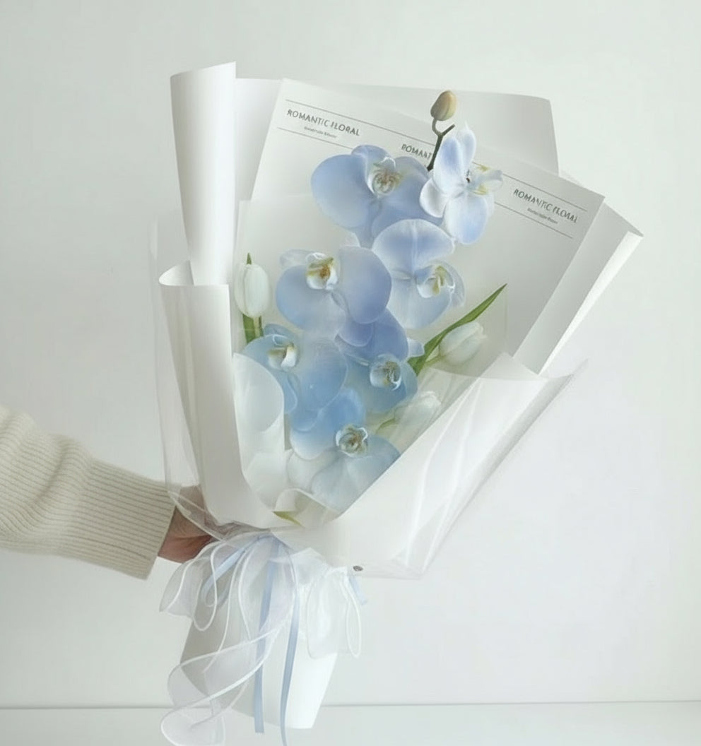 Ramo de orquídeas azules envuelto en papel blanco con lazo de organza, presentación elegante y moderna – The Prestige Roses Madrid