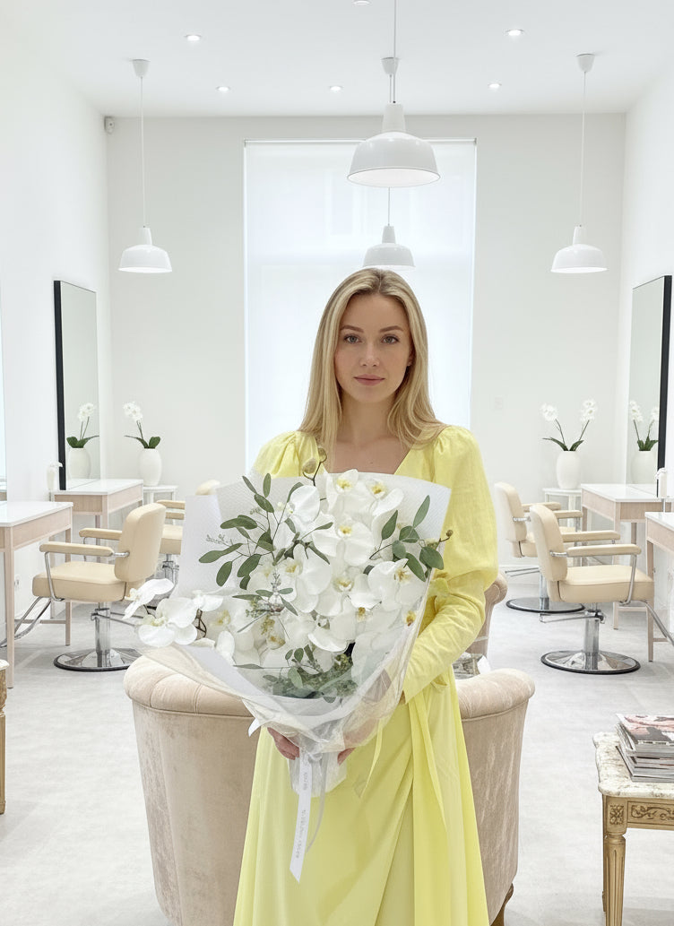 Ramo de orquídeas blancas frescas con eucalipto, envuelto en papel blanco de lujo y sostenido por una persona con vestido amarillo – The Prestige Roses Madrid