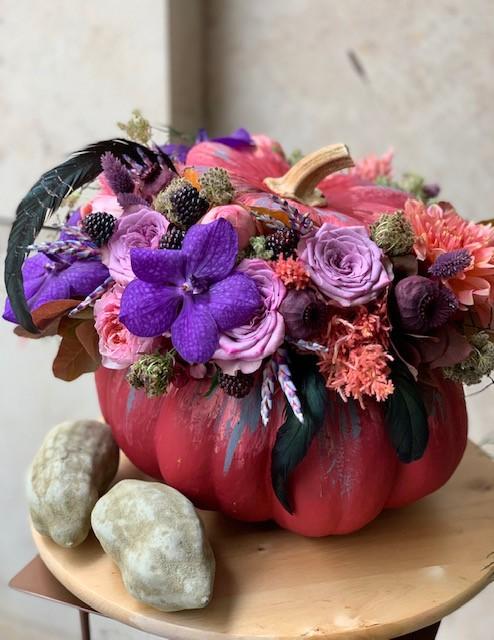 Arreglo floral en calabaza roja con flores violetas y rojas, diseño artesanal de otoño.