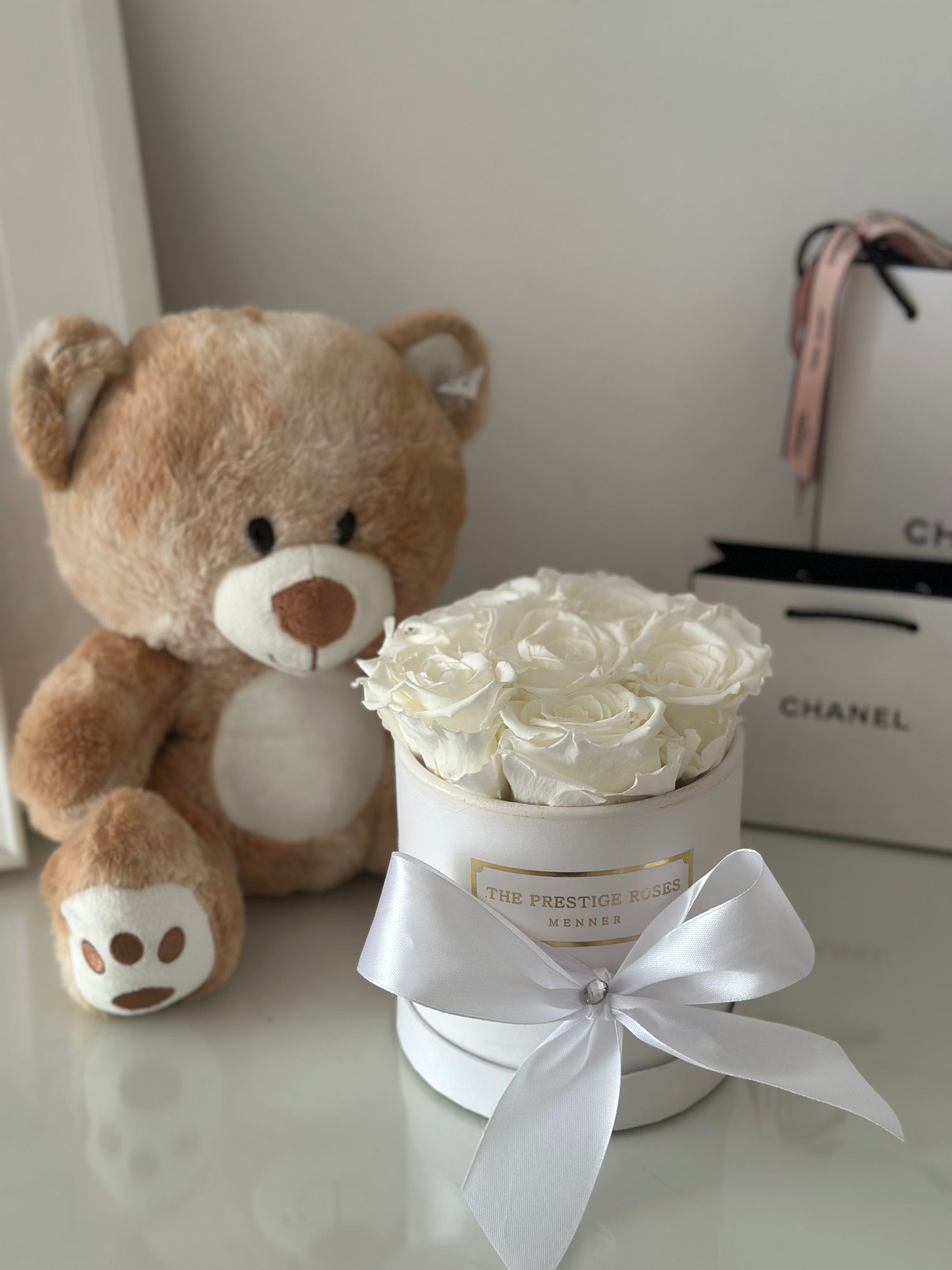 Caja de rosas blancas con lazo de seda, acompañada de un tierno oso de peluche. Un regalo elegante y delicado, ideal para ocasiones especiales.
