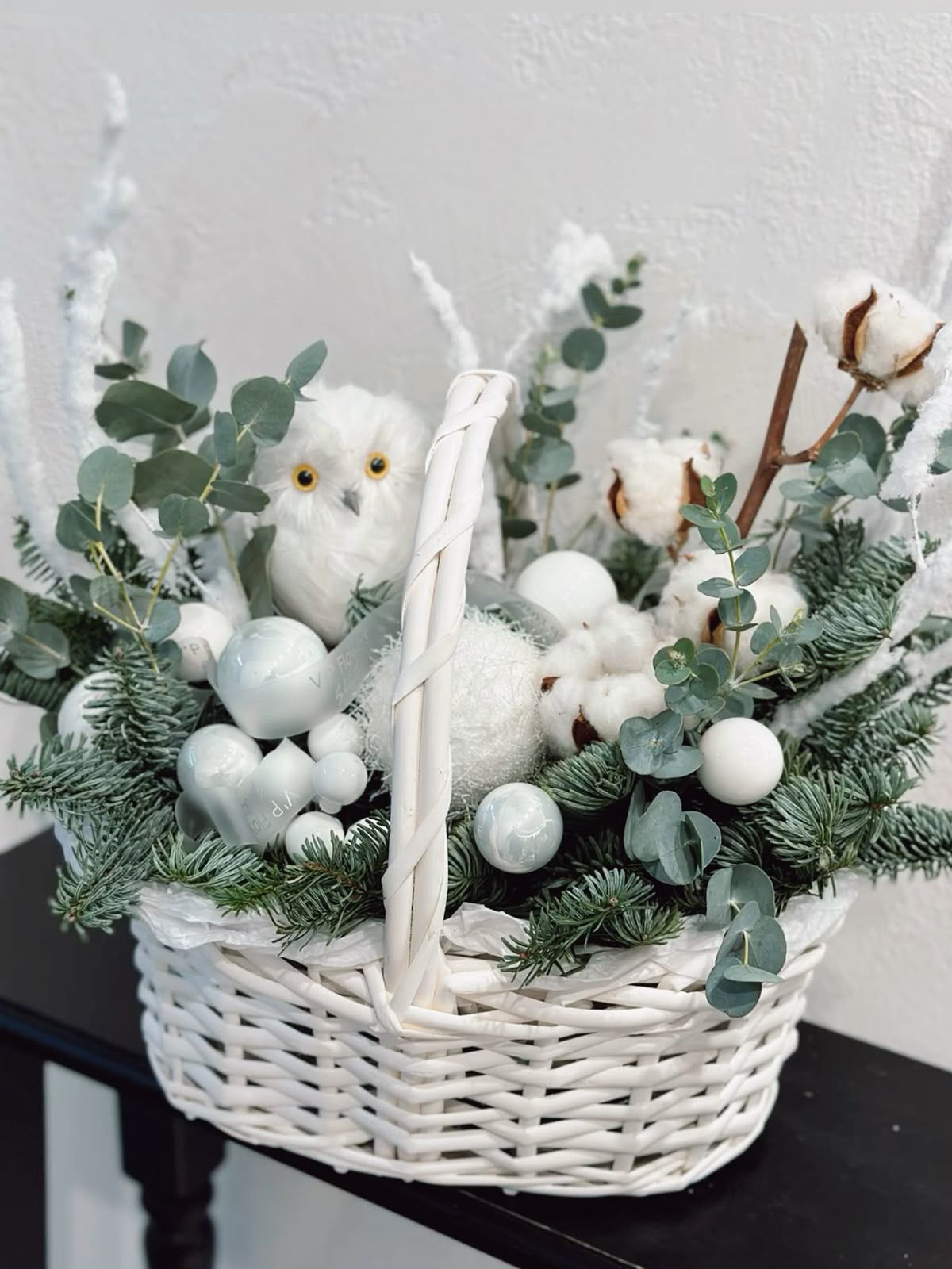 Cesta navideña en tonos blancos con eucalipto, ramas de abeto, algodón natural y adornos festivos.