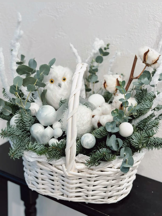 Cesta navideña en tonos blancos con eucalipto, ramas de abeto, algodón natural y adornos festivos.