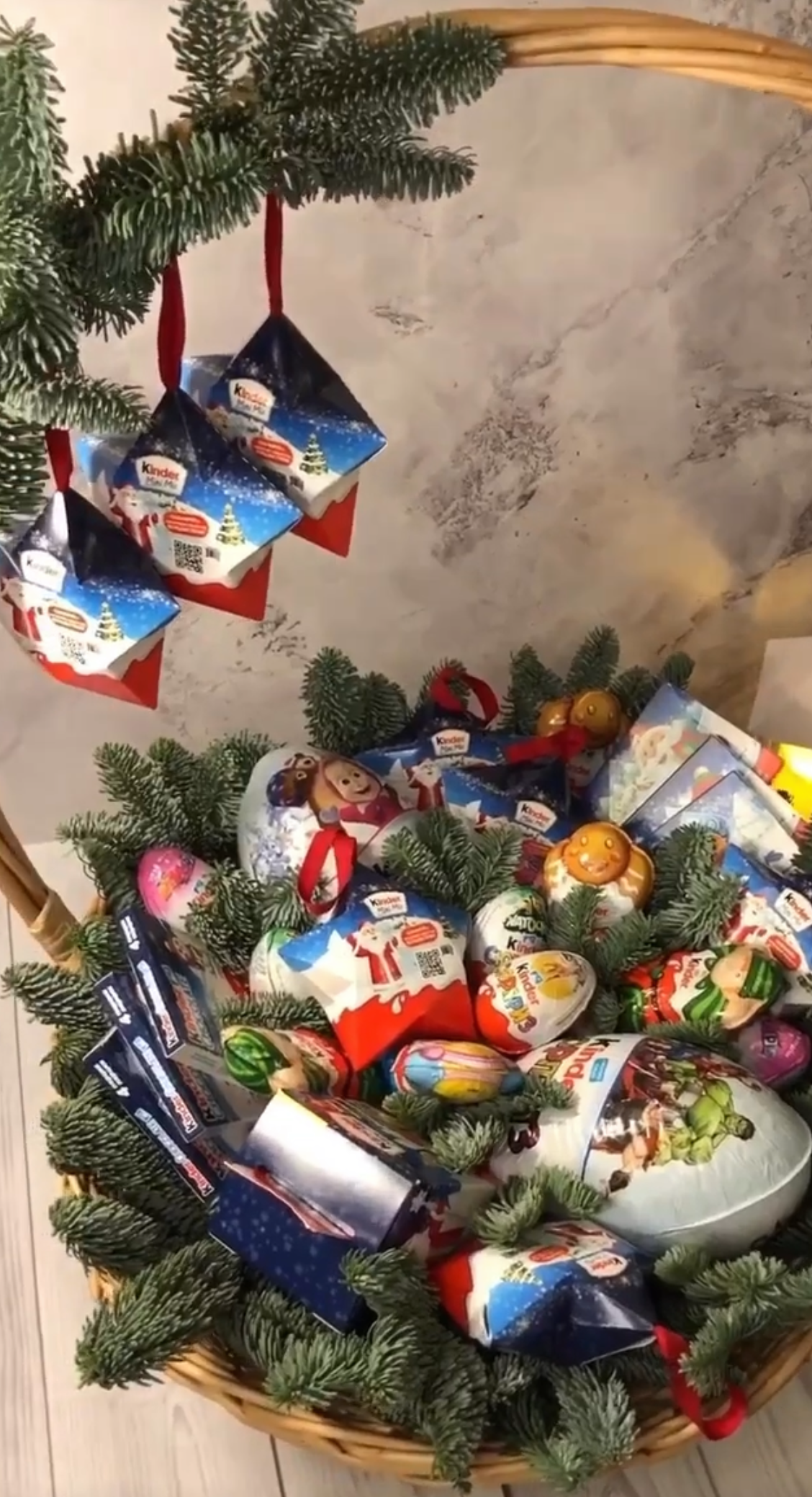 Cesta navideña decorada con chocolates Kinder, Nutella y Ferrero, adornada con ramas de abeto y detalles festivos.