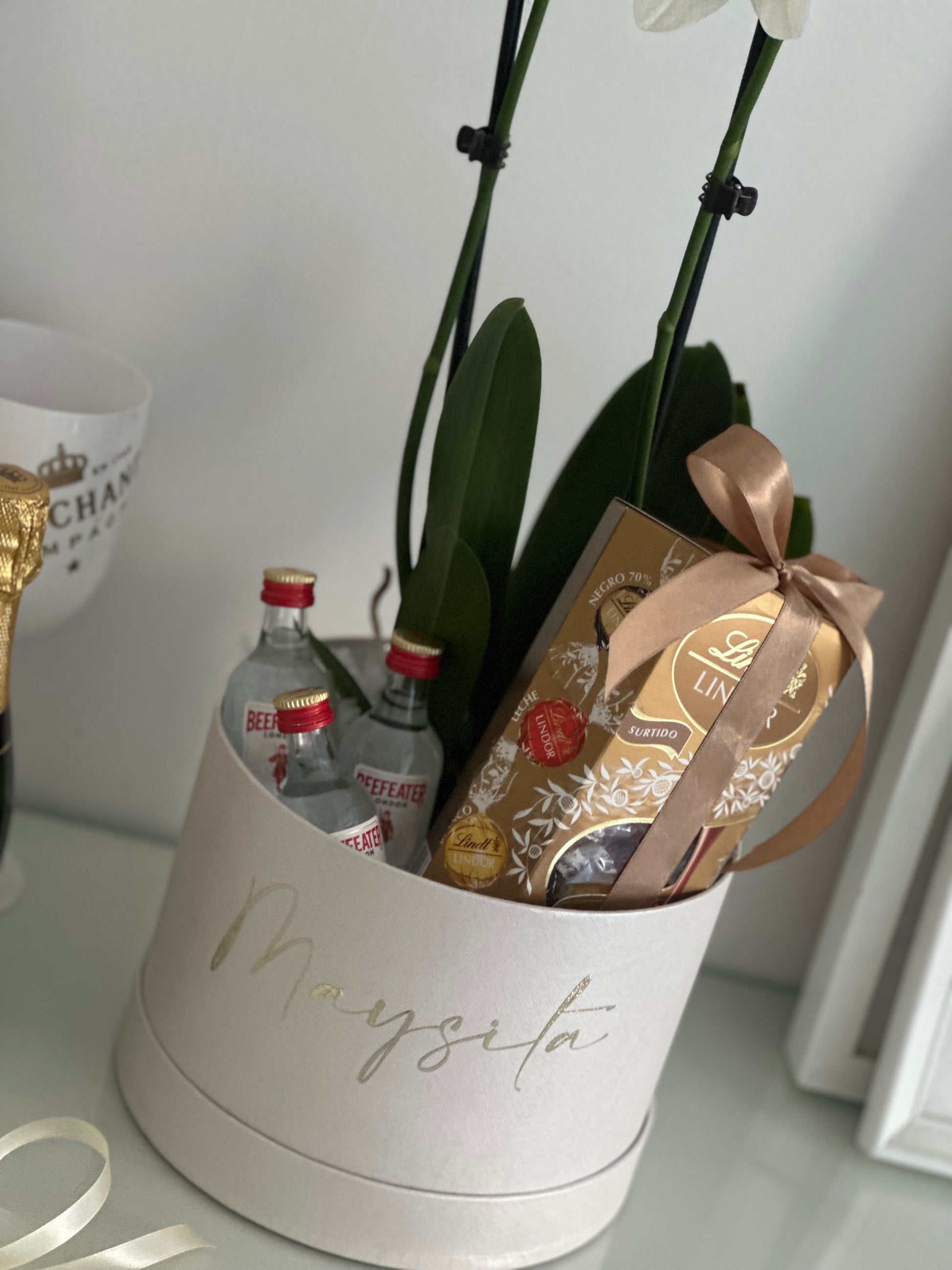 Sorprende con un regalo elegante y exclusivo que combina una orquídea blanca Phalaenopsis de larga duración, mini ginebras premium y una selección de chocolates Lindt. Presentado en una caja personalizada con nombre, es el detalle perfecto para cumpleaños, aniversarios, agradecimientos y ocasiones especiales en Madrid.