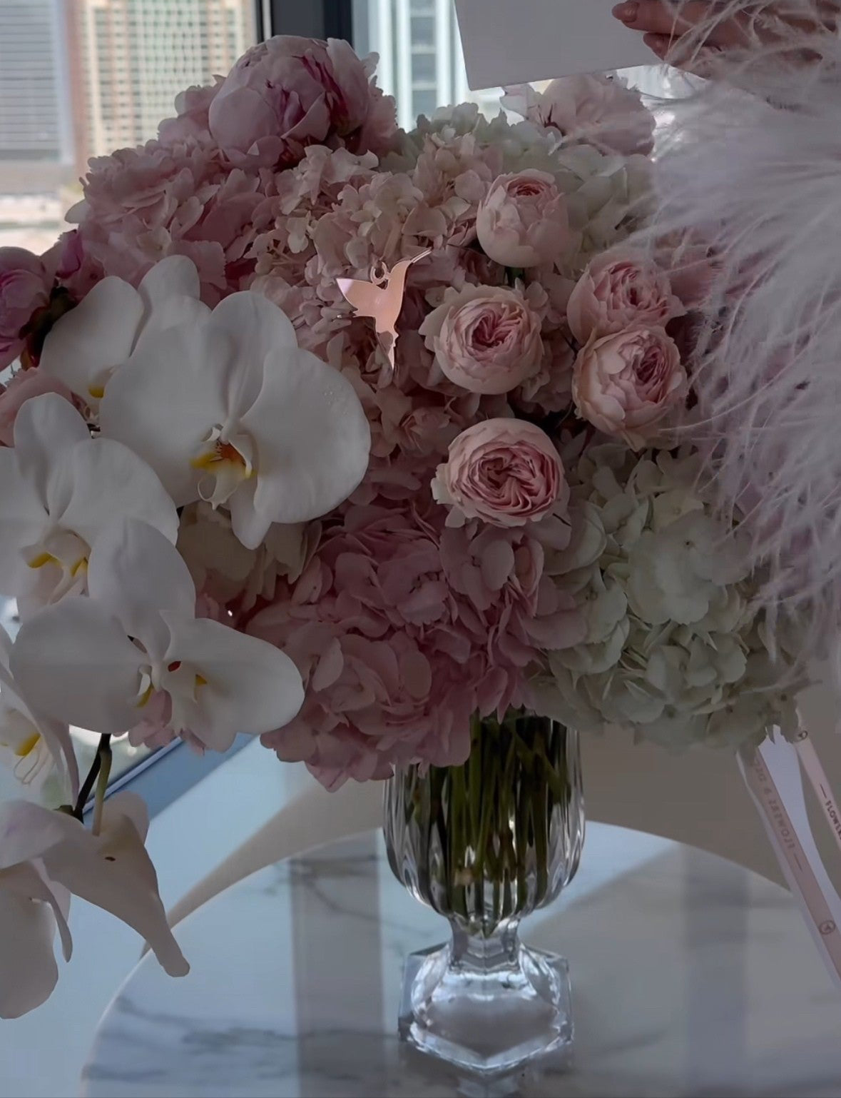 Arreglo floral de lujo en tonos blancos y rosas con orquídeas frente a skyline urbano – decoración exclusiva en interior VIP.