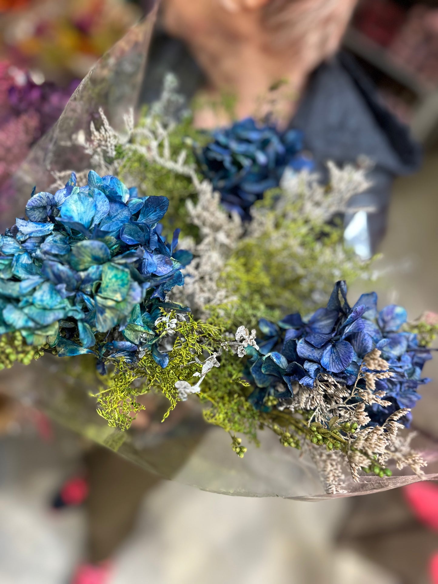 Composición de flores preservadas  azules y verdes y colores naturales y follaje silvestre.