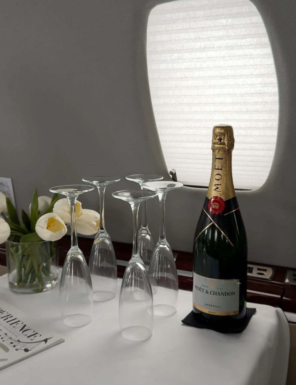 Botella de Moët & Chandon con copas de champagne en una mesa de jet privado decorada con flores blancas.