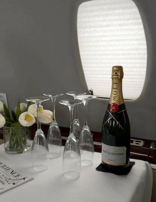 Botella de Moët & Chandon con copas de champagne en una mesa de jet privado decorada con flores blancas.