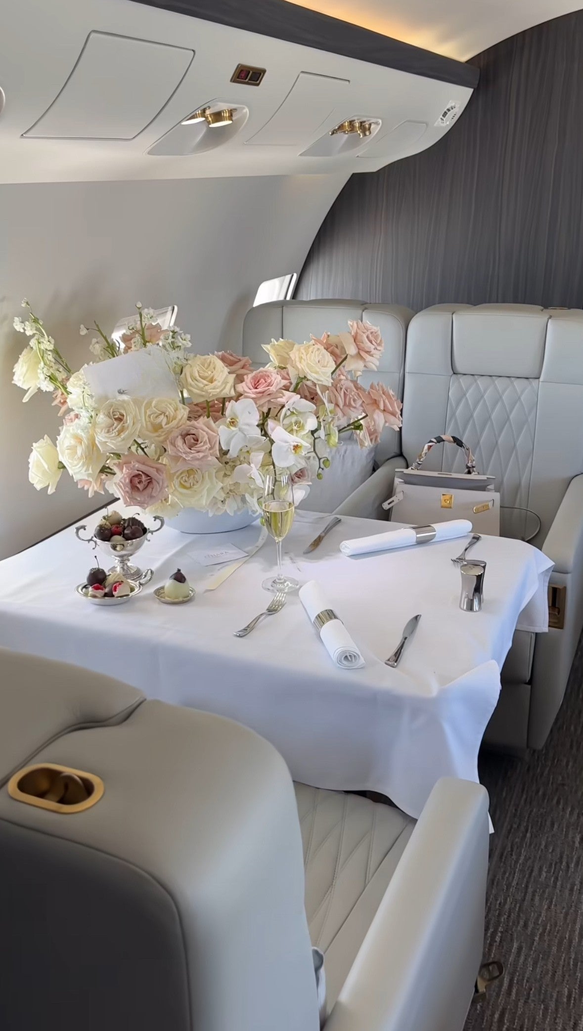 Mesa decorada con flores de lujo en tonos nude, champagne y crema, a bordo de un jet privado con interior de piel blanca.