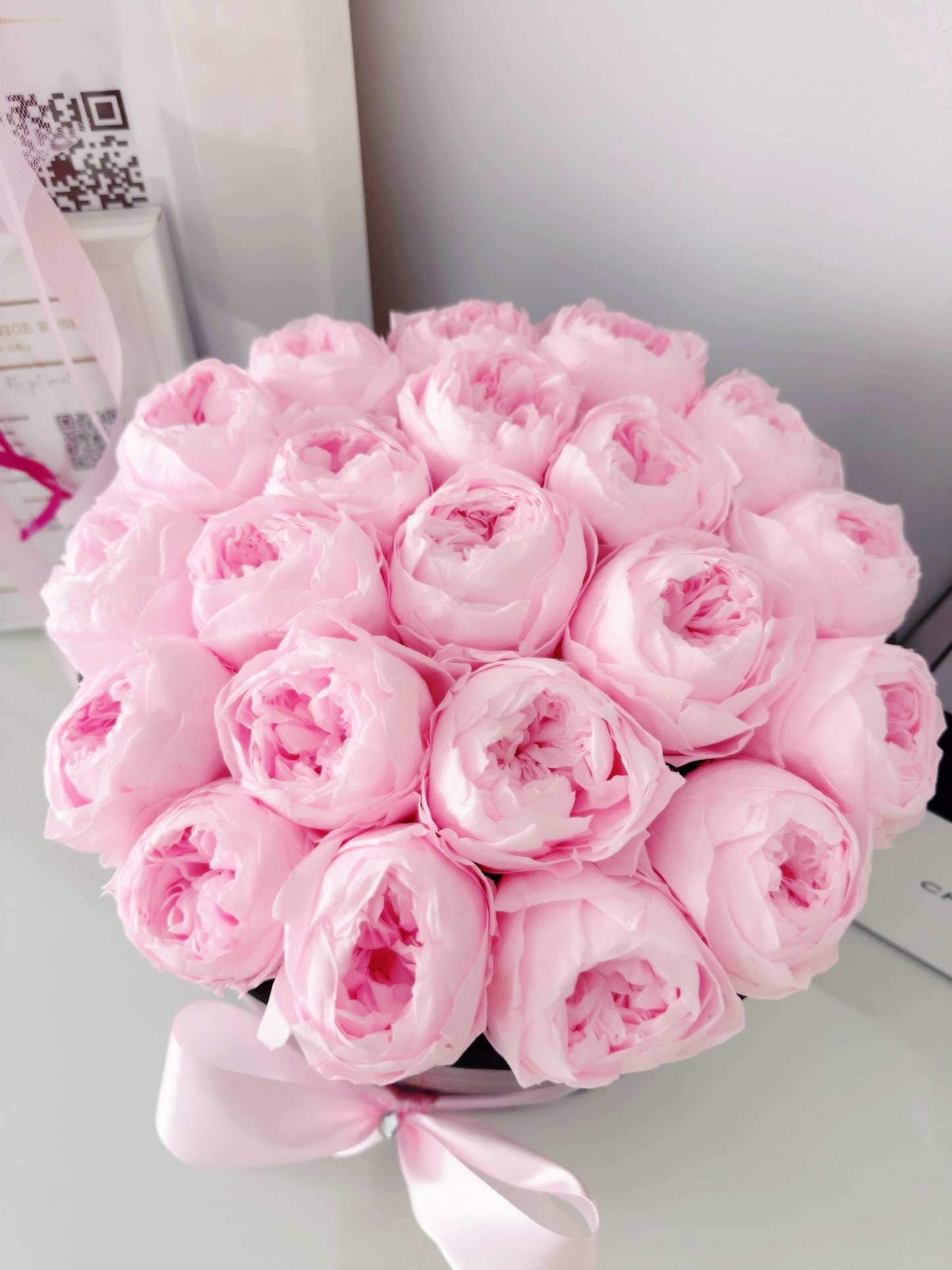 Caja de peonías preservadas en color rosa claro con lazo blanco.