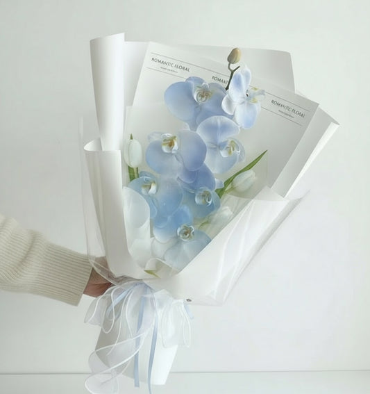 Ramo de orquídeas azules envuelto en papel blanco con lazo de organza, presentación elegante y moderna – The Prestige Roses Madrid