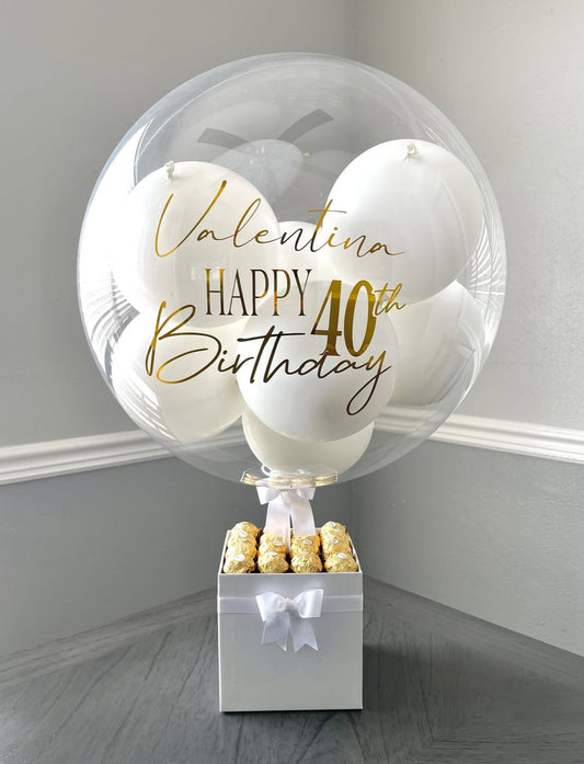 Set de regalo blanco y dorado con globo personalizado y chocolates Ferrero Rocher – lujo y elegancia de The Prestige Roses Madrid.  
White and gold personalized balloon gift set with Ferrero Rocher chocolates – luxury detail by The Prestige Roses Madrid.